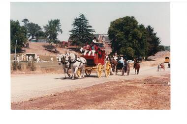 Coach drawn by two white horses on dirt road, school and bowling green in background.