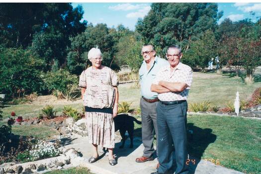 A colour photograph of three members of the Buninyong and District Historical Society on an excursion to Green Hills in March 1996 in a garden surrounded by trees