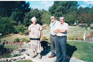 A colour photograph of three members of the Buninyong and District Historical Society on an excursion to Green Hills in March 1996 in a garden surrounded by trees