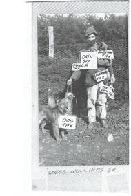 Man in swagman's costume, covered with signs, holding a dog on lead. 