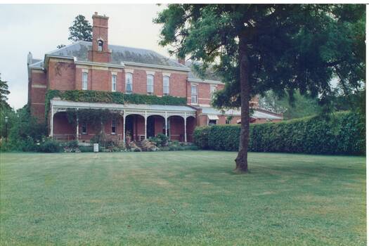 Colour photograph of the croquet lawn and Mt Boninyong Homestead, the side verandah and hedging in the background