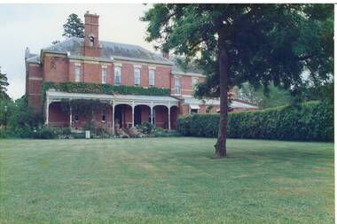 Colour photograph of the croquet lawn and Mt Boninyong Homestead, the side verandah and hedging in the background