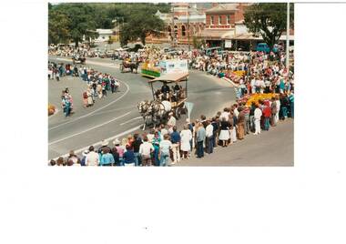 Looking down at procession, horse-drawn carts, crowds lining sides of the road, old brick buildings in thje background.