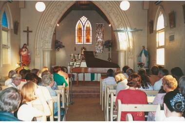 Photograph colour of audience in old Catholic Church Buninyong, religious statues left and right of grand piano, altar and stained glass window at rear