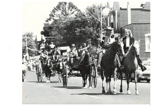 Mounted riders and horse drawn vehicles in procession.