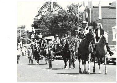 Mounted riders and horse drawn vehicles in procession.