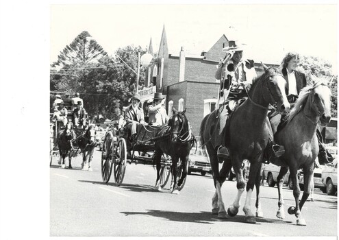 Procession in period dress, man and woman on horseback leading, followed carriage with one horse driven by two men, behind them a two horse carriage