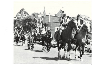 Procession in period dress, man and woman on horseback leading, followed carriage with one horse driven by two men, behind them a two horse carriage