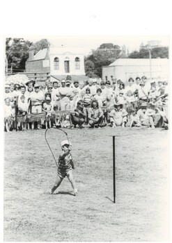 Black and White image of Daniel Young aged 4 of Toongabbie in Whip Cracking competition showing spectators and the 2nd storey of Old Eagle Hotel in background without balcony