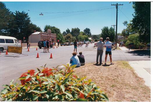 Looking down road to intersection, group of cyclists speeding around the corner.