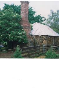 Colour photograph of part of the original stone homestead building of the Scott family on Mt Boninyong estate surrounded by large trees featuring a large brick chimney and corrugated iron roof