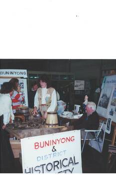 Display table at History Fair, two ladies standing and one man seated, Display boards and signage.