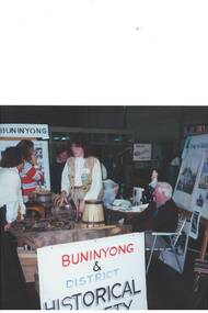 Display table at History Fair, two ladies standing and one man seated, Display boards and signage.
