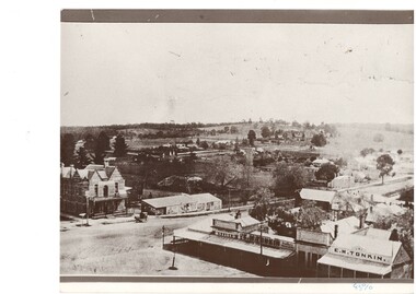 View looking down on intersection in country townhotel on left, shops lower right, fields and low hills in distance.