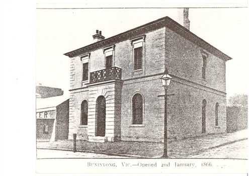 Two story rendered bank building, slightly extended entrance portico  topped with iron balcony, ground floor flanked by arched windows, upper floor rectangular windows, gas lamp on corner of footpath.