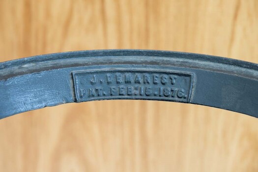 A raised inscription on the upper side of the top ring of the gasometer that reads "J. DEMAREST//PAT.FEB.15.1876". The inscription is enclosed in a raised rectangle.