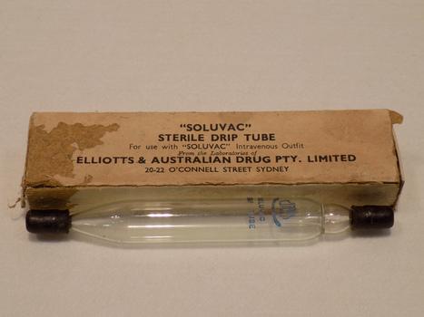 Glass tube with black rubber stopper at each end, sitting in front of a discoloured and stained storage box in the background.
