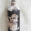 A black cylinder with white painted neck, and degraded label on the front with rust marks and missing parts.
