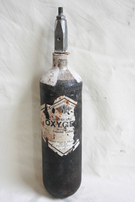 A black cylinder with white painted neck, and degraded label on the front with rust marks and missing parts.