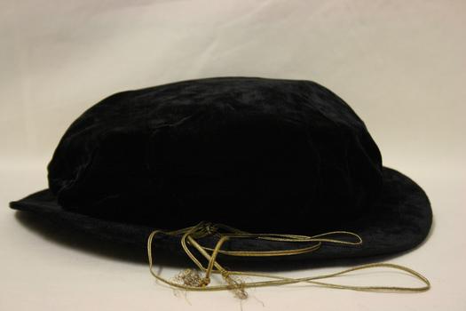 A navy blue velvet cloth bonnet with stiffened brim covered in same fabric as bonnet with a gold cord and tassles tied around it.