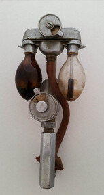 Two glass bulbs are attached to a metal connector, with a red rubber tube running through the centre point, over a gauge/