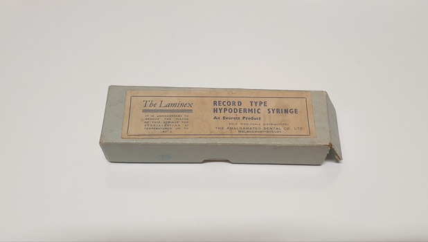 Greenish grey cardboard box with manufacturer's label stuck on the top