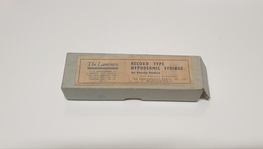 Greenish grey cardboard box with manufacturer's label stuck on the top
