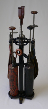 Cast iron stand with holders for oxygen and nitrous oxide cylinders, along with face mask and rebreather bags.