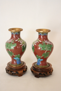 Twin vases decorated ornately in red with floral designs in green, blue, and white on carved wooden bases.