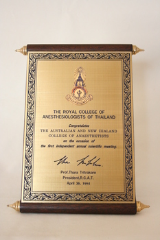 A brass and wood plaque in the design of a scroll.