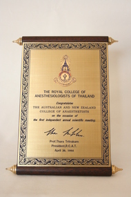 A brass and wood plaque in the design of a scroll.
