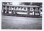A man in work clothes bends down to tend to the tracks of a vintage tramcar. The tram is open-sided, revealing multiple windows and doors.