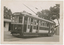 Shows tram numbered 29. The tram has several windows and appears to be stopped at a depot, with a building to the left and trees in the background.