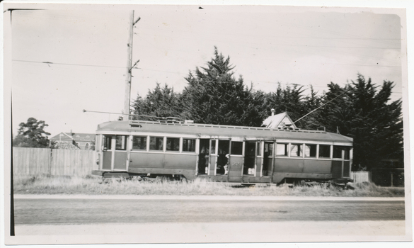 A vintage tramcar with number 22 visible on its side, stopped on grassy land next to a road, with a wooden fence and trees in the background.