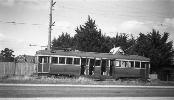 A vintage tramcar with number 22 visible on its side, stopped on grassy land next to a road, with a wooden fence and trees in the background.