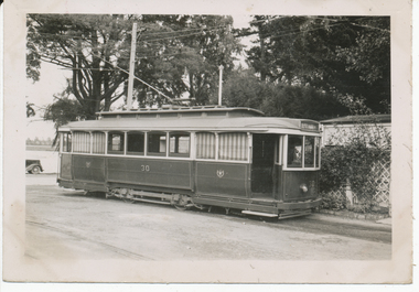 tramcar numbered 30 with multiple windows and an open door, parked on tracks outdoors with trees and a building in the background.
