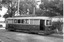 tramcar numbered 30 with multiple windows and an open door, parked on tracks outdoors with trees and a building in the background.