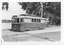 A vintage electric tram, number 17, with "Victoria St" displayed on its front, is parked on a track next to a body of water and trees. A vintage car is visible parked behind the tram.