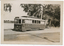 A vintage electric tram, number 17, with "Victoria St" displayed on its front, is parked on a track next to a body of water and trees. A vintage car is visible parked behind the tram.