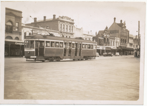 A historic tram car travels down a street lined with brick buildings, some featuring awnings and signs for businesses like "Union Hotel" and "Tarax Bar."