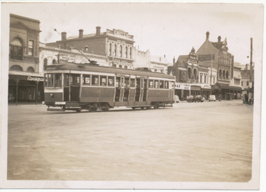 A historic tram car travels down a street lined with brick buildings, some featuring awnings and signs for businesses like "Union Hotel" and "Tarax Bar."