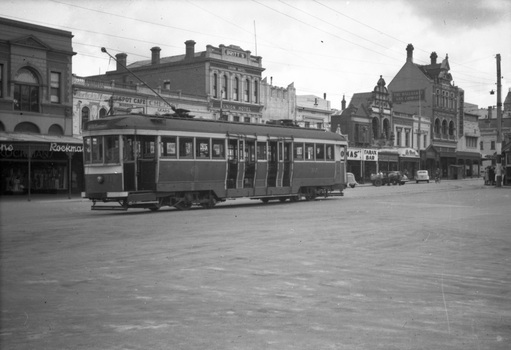 A historic tram car travels down a street lined with brick buildings, some featuring awnings and signs for businesses like "Union Hotel" and "Tarax Bar."