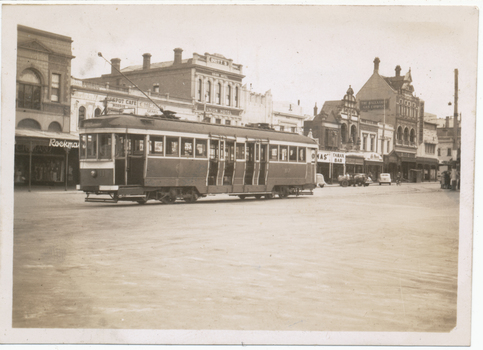 A historic tram car travels down a street lined with brick buildings, some featuring awnings and signs for businesses like "Union Hotel" and "Tarax Bar."