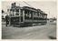 A decorated vintage tram numbered 28, with a driver in uniform stepping onto the platform, is parked on a street, adorned with Union Jack flags and ornate banners.
