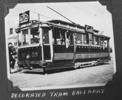 A decorated vintage tram numbered 28, with a driver in uniform stepping onto the platform, is parked on a street, adorned with Union Jack flags and ornate banners.