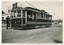 A decorated vintage tram numbered 28, with a driver in uniform stepping onto the platform, is parked on a street, adorned with Union Jack flags and ornate banners.