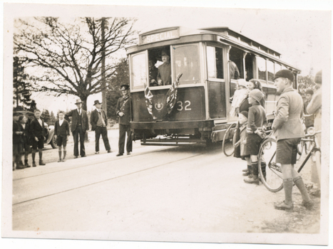 A vintage tramcar labeled "SPECIAL" with the number 32 on its side, stopped on tracks beside a group of men and children, with a few bicycles nearby.
