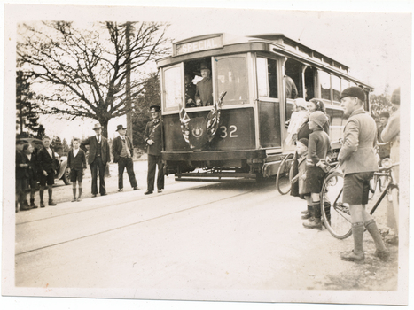 A vintage tramcar labeled "SPECIAL" with the number 32 on its side, stopped on tracks beside a group of men and children, with a few bicycles nearby.