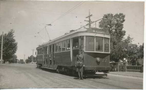 Tramcar with destination of "Mt Pleasant" and numbered 22, with a conductoress standing beside it on a street in front of trees and a stone wall.