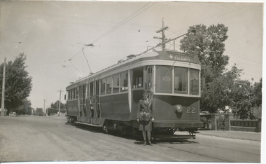 Tramcar with destination of "Mt Pleasant" and numbered 22, with a conductoress standing beside it on a street in front of trees and a stone wall.